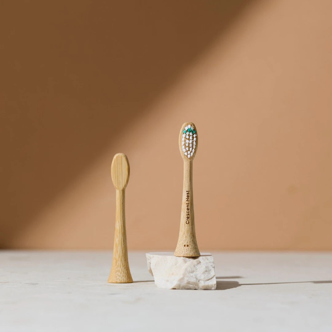 Two bamboo toothbrushes on a light surface with a warm brown background
