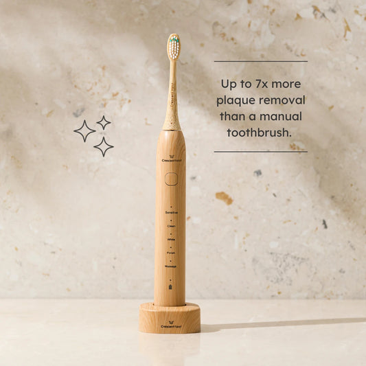 Crescent Nest bamboo electric toothbrush on charging base with text highlighting up to 7x more plaque removal than a manual toothbrush.