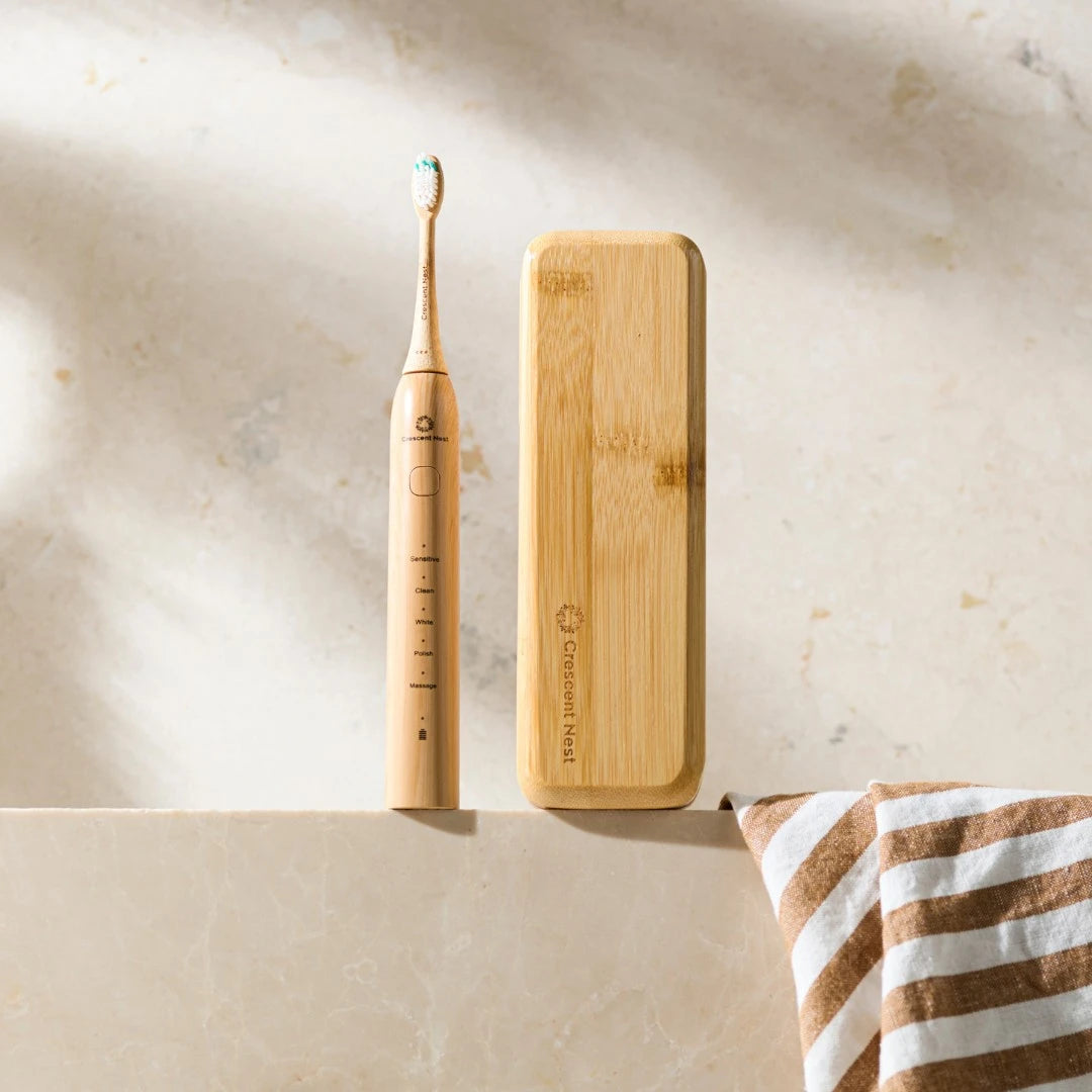 Bamboo electric toothbrush and its charging case on a marble surface with a striped towel.