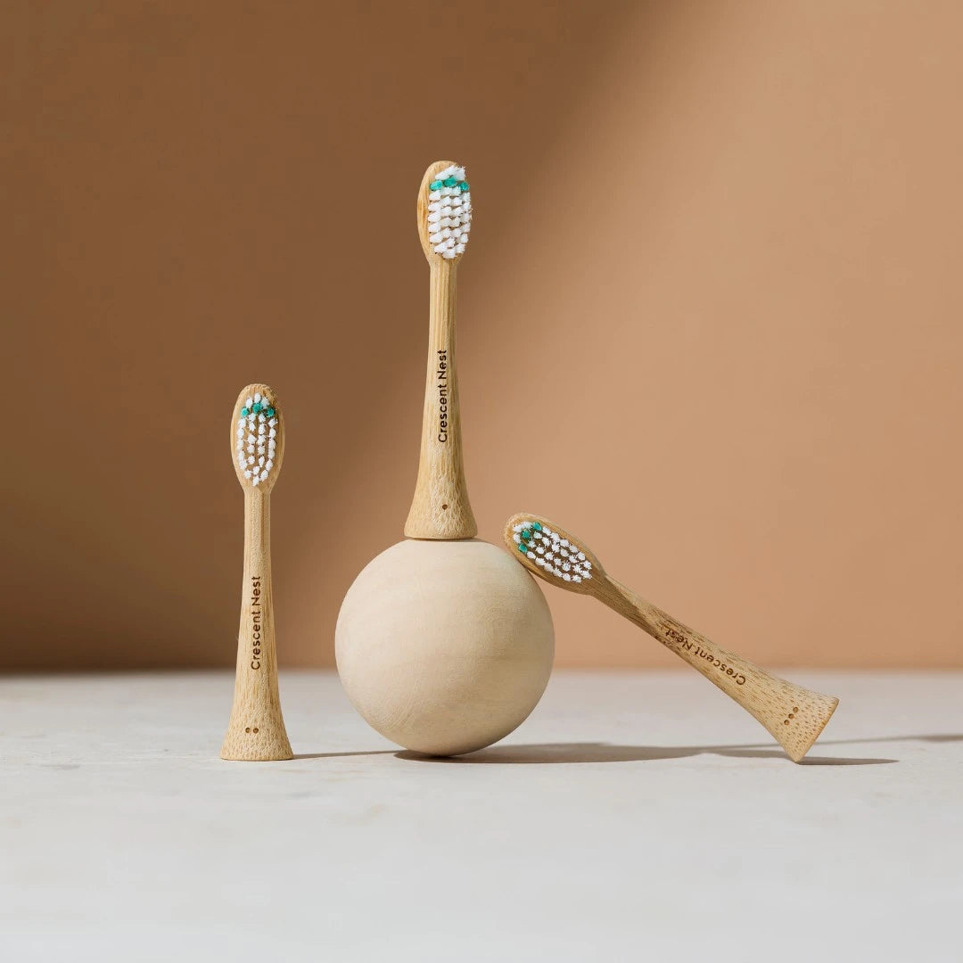 Three bamboo toothbrushes with teal bristles on a beige surface and brown background