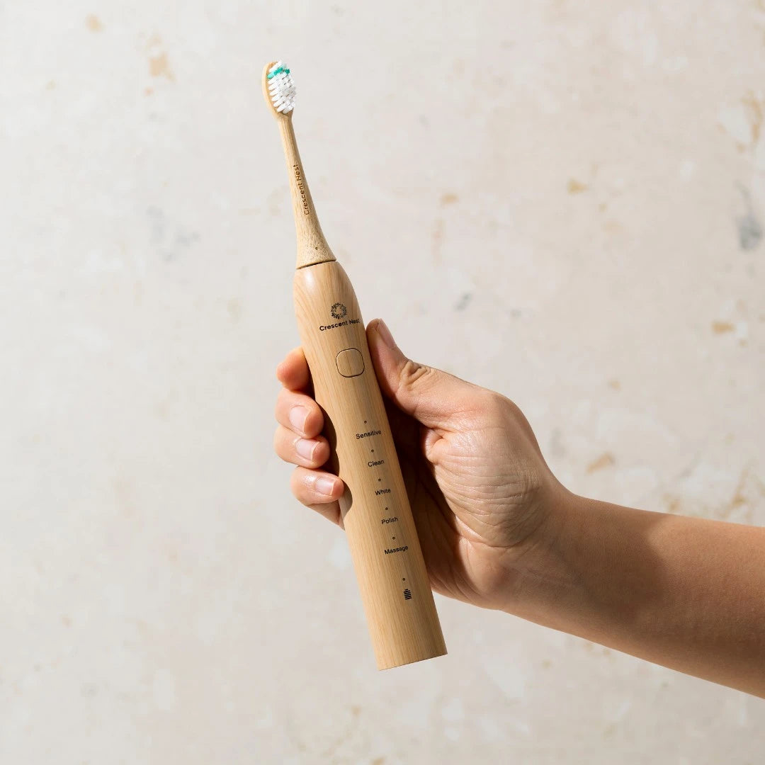 Hand holding a bamboo electric toothbrush against a light background