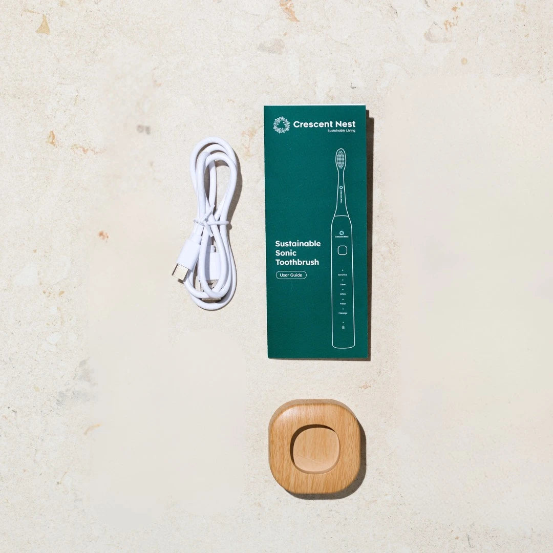 Crescent Nest sustainable sonic toothbrush set with packaging, charger, and wooden case on a beige surface.