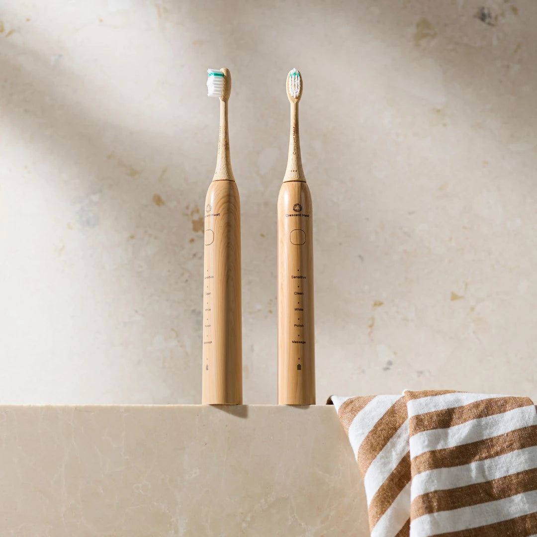 Two bamboo electric toothbrushes on a beige surface with a striped towel.