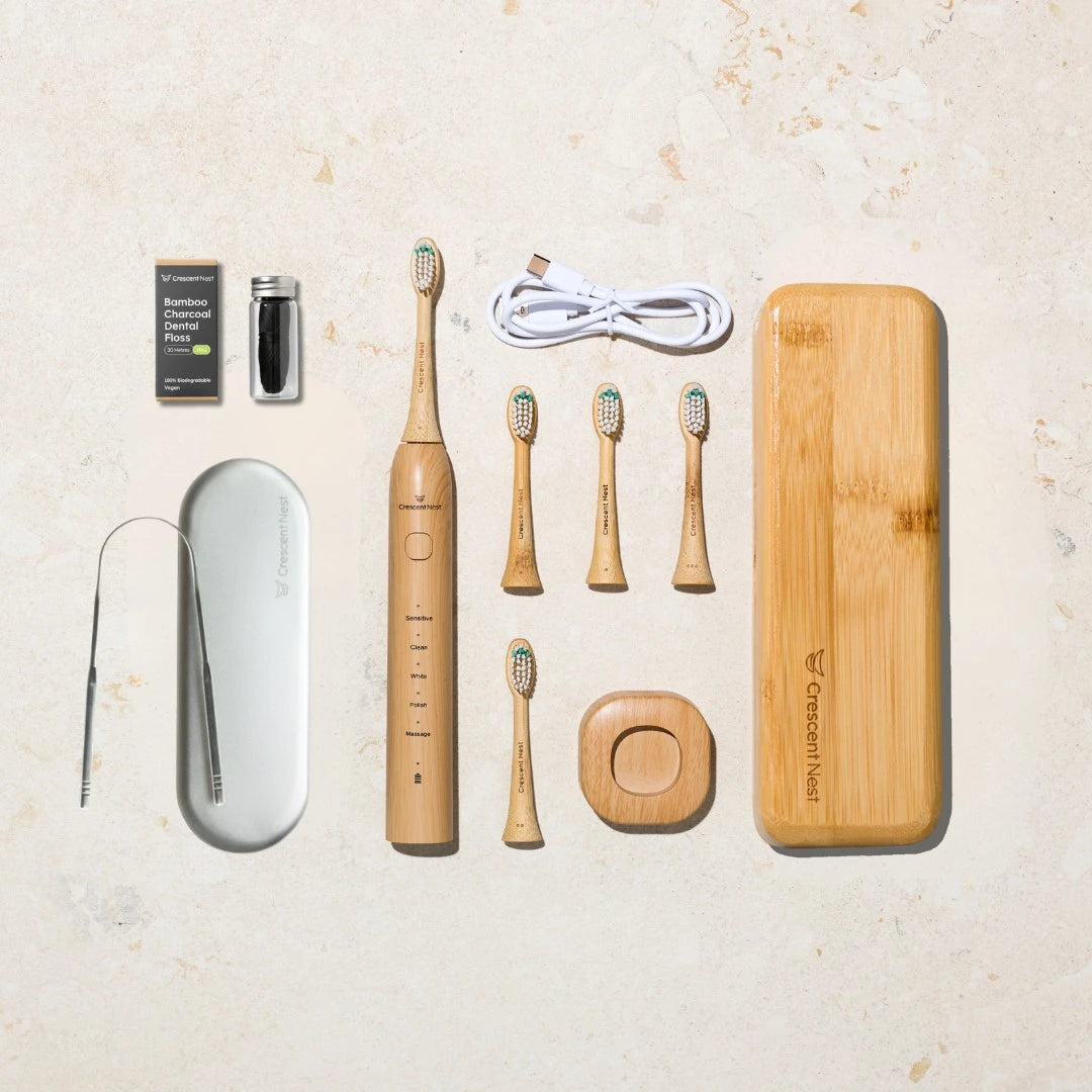 Set of crescent nest sonic bamboo toothbrushes, charging case, and other dental care products on a light background
