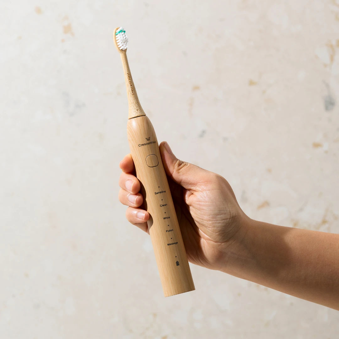 Hand holding the Crescent Nest bamboo electric toothbrush, showing its natural design and cleaning modes.