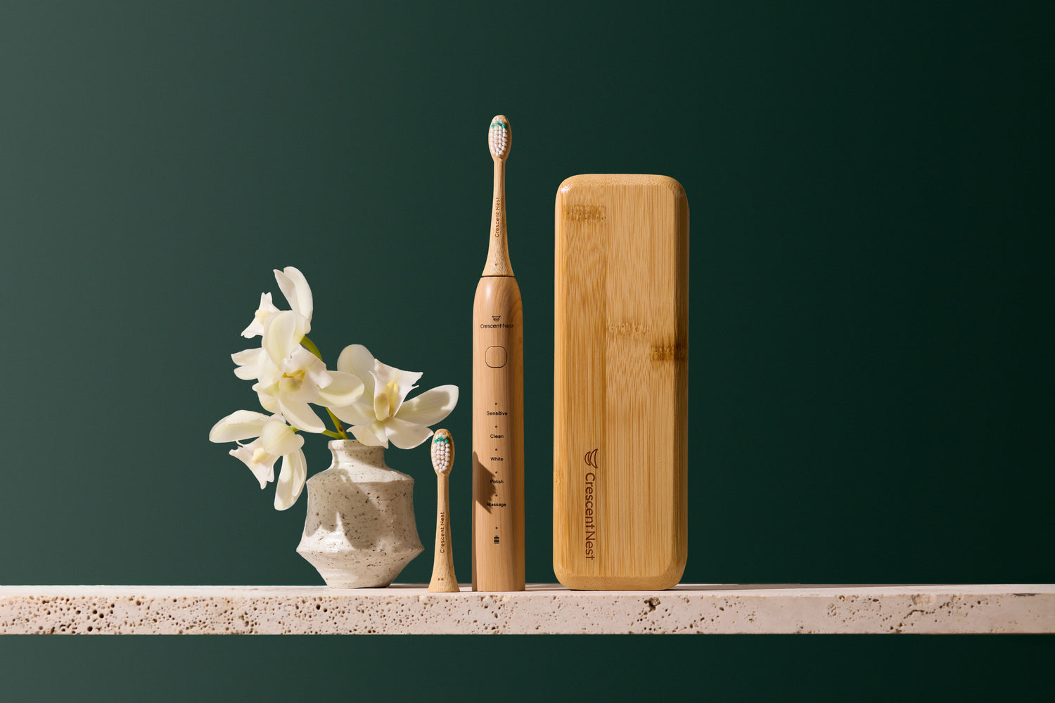 Crescent Nest bamboo electric toothbrush with replacement head, travel case, and white flowers styled on a bathroom shelf.