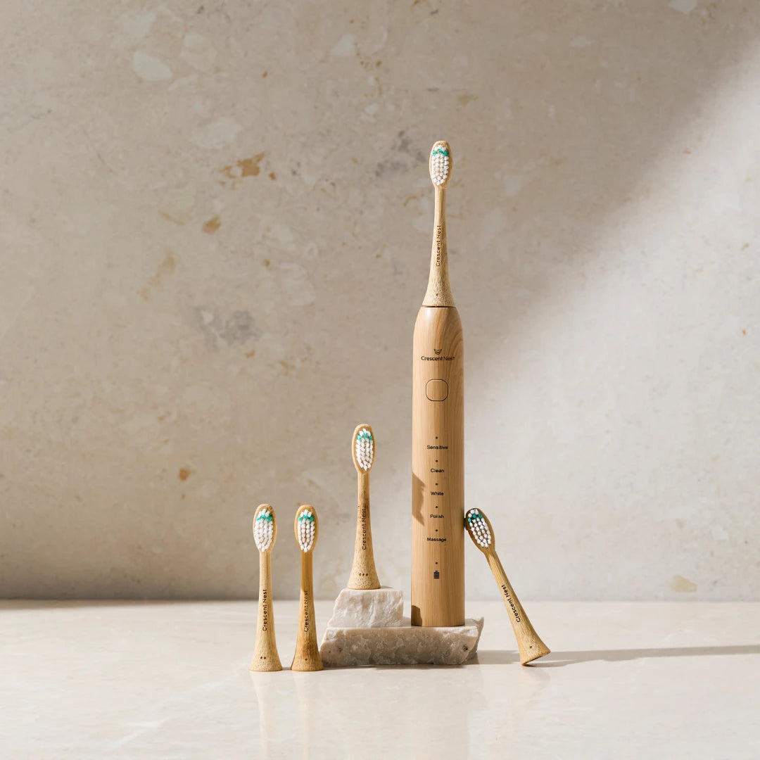 Crescent Nest bamboo electric toothbrush displayed with multiple replacement bamboo brush heads on a bathroom surface.