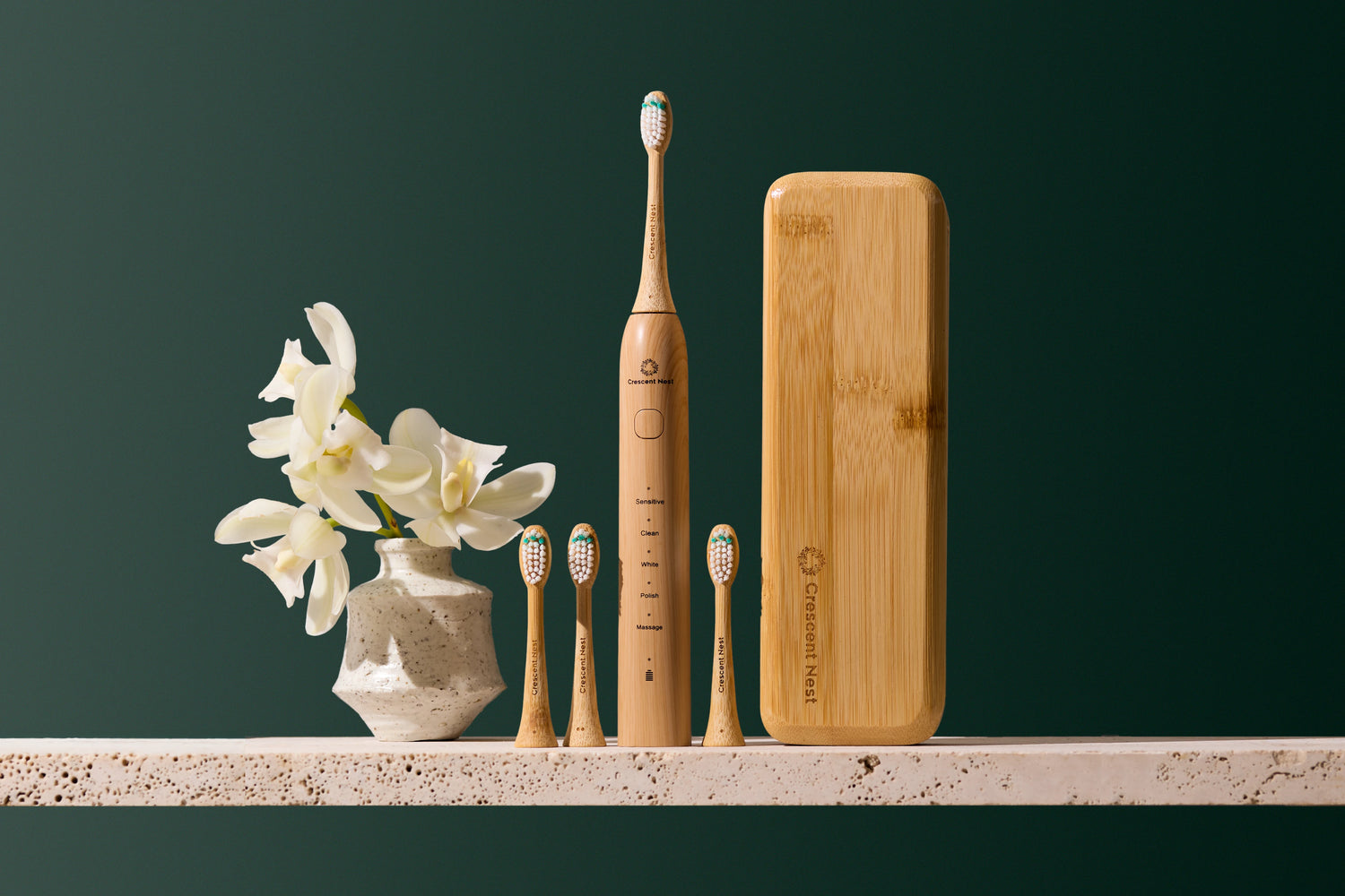 Set of bamboo toothbrushes and a bamboo case on a dark green background with a vase of flowers.