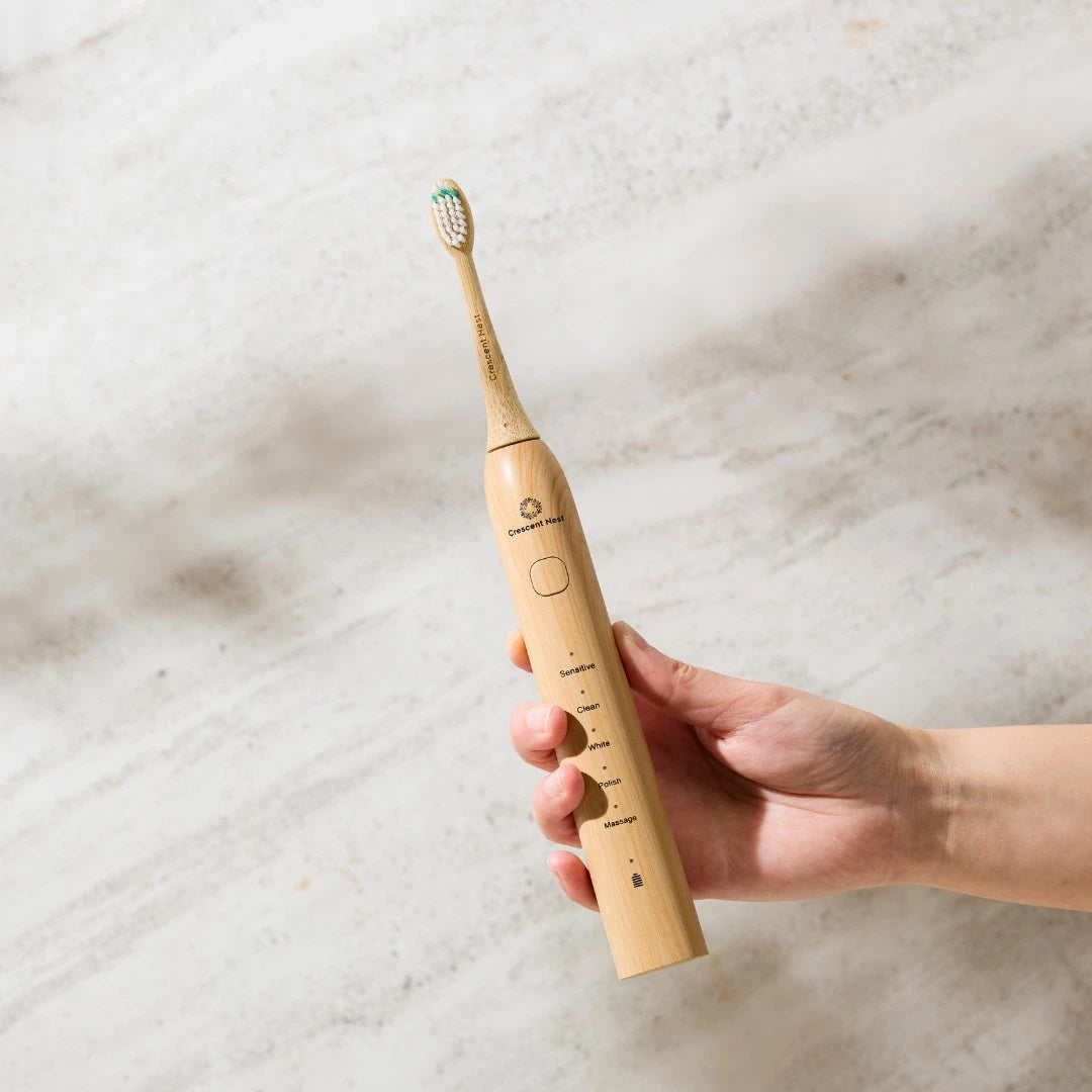Hand holding a beige electric toothbrush on a marble surface